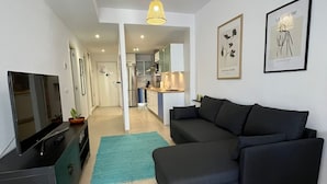Een moderne woonkamer met een grote zwarte hoekbank, een flatscreen televisie en een keuken op de achtergrond.