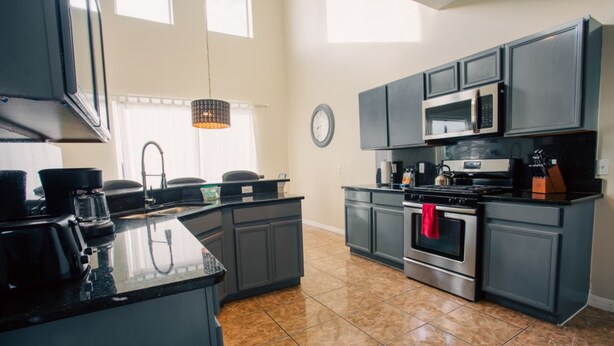 A modern kitchen with dark cabinetry, a stainless steel oven, and a microwave. - Cheerful 5 bed - 4 Bath Spacious Home (Kissimmee)