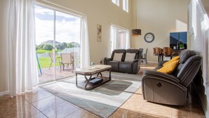 A spacious living room with a sliding glass door leading to a patio, a reclining chair, a coffee table, and a massage chair. - Cheerful 5 bed - 4 Bath Spacious Home (Kissimmee)