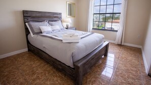 A neatly made bed with a wooden headboard, a bedside lamp, and a window with curtains. - Cheerful 5 bed - 4 Bath Spacious Home (Kissimmee)