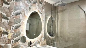 Un baño con pared de piedra con diseño de hojas, un espejo redondo, un lavabo y una ducha.
