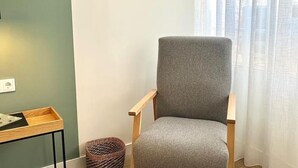 Una habitación con una silla tapizada de gris, una mesa de madera con una bandeja, un enchufe y una cesta de mimbre.