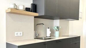 Una cocina moderna con armarios oscuros, encimera clara, pileta de acero inoxidable y una ventana pequeña.