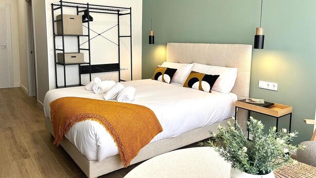 Un dormitorio moderno con una cama, una estantería empotrada, una planta en maceta y una mesita de noche.