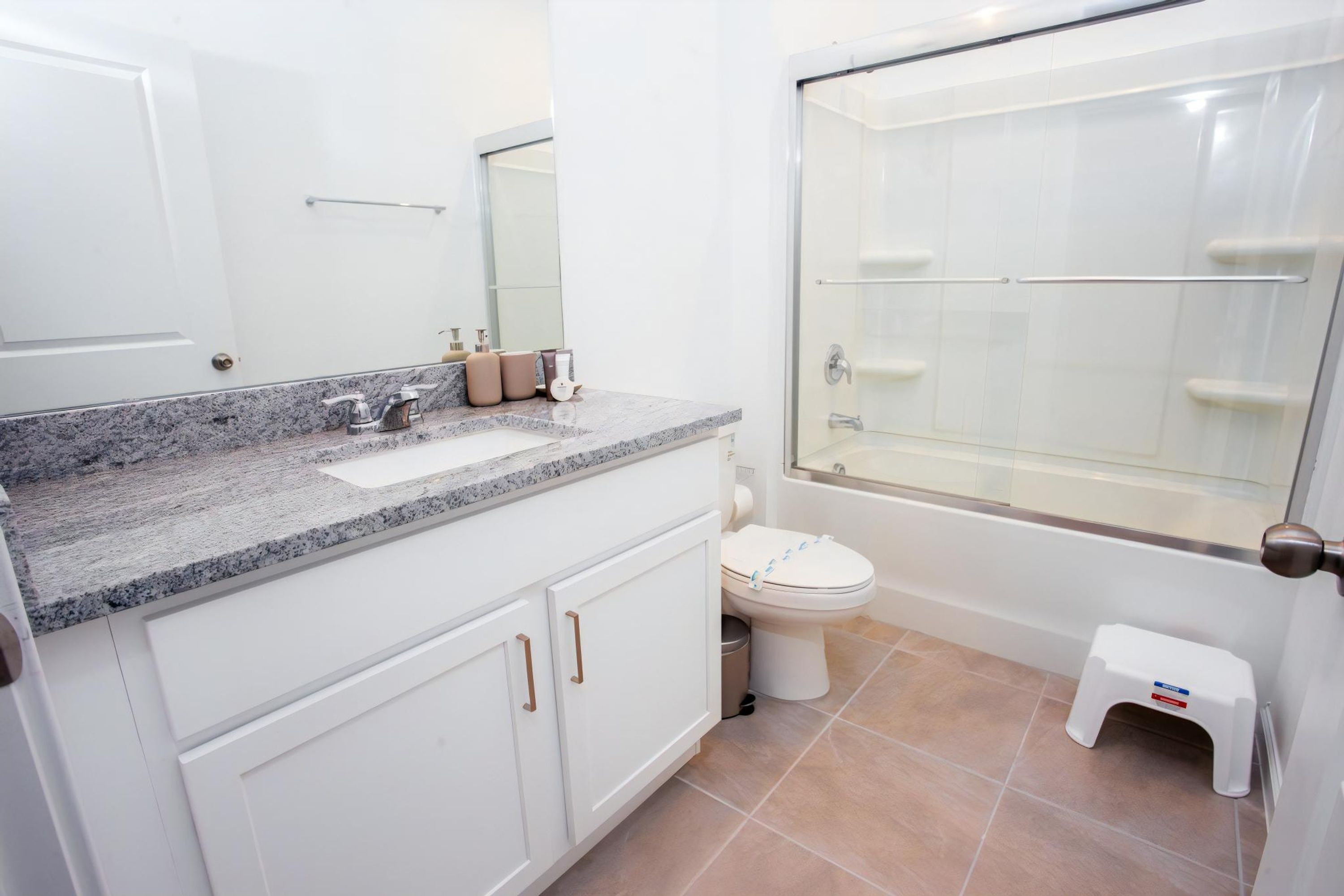 Ein Badezimmer mit Granitplatte, weißen Schränken, Toilette und einer Duschkabine.