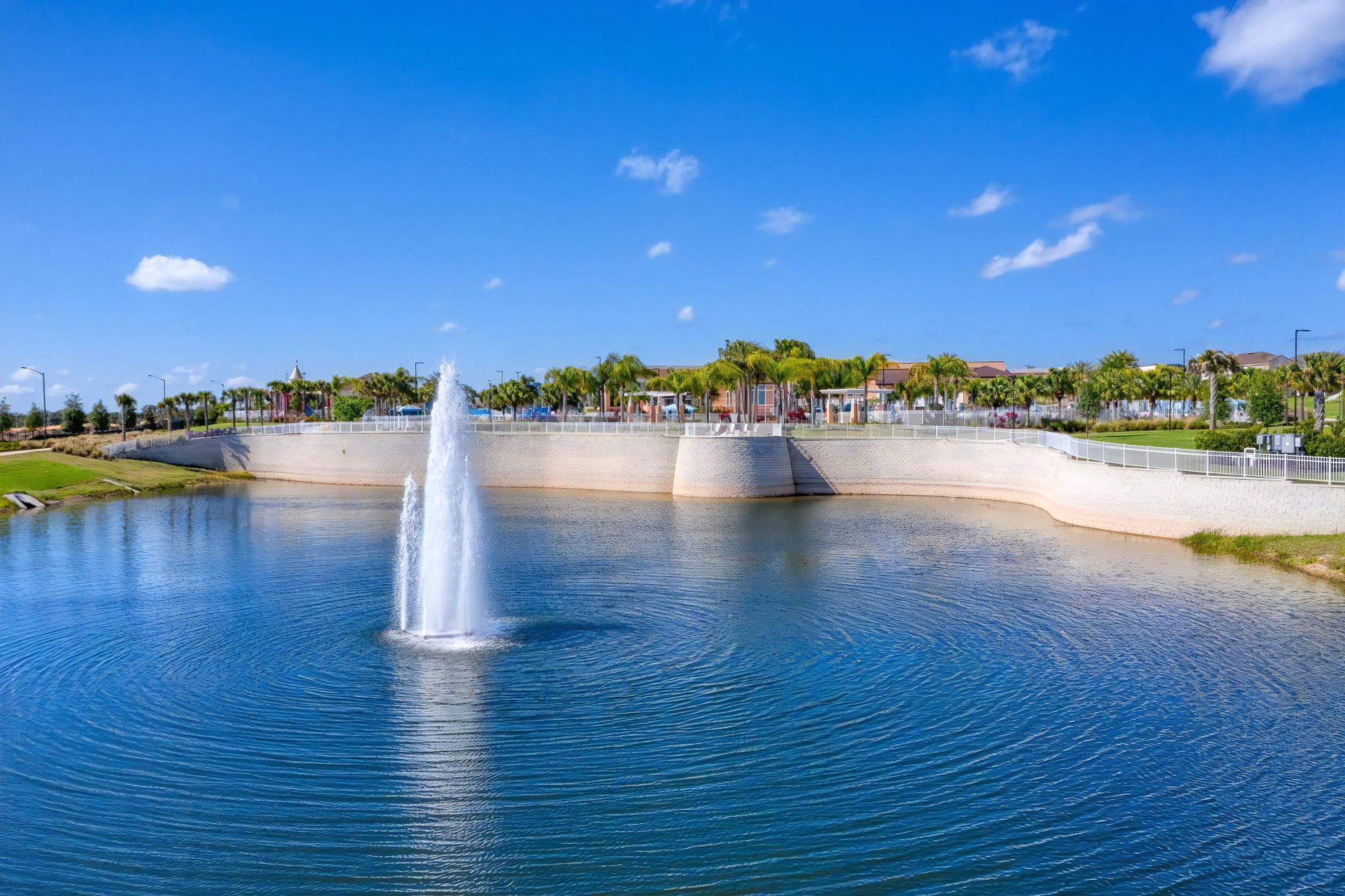 A large body of water with a central fountain, surrounded by a concrete barrier and palm trees.