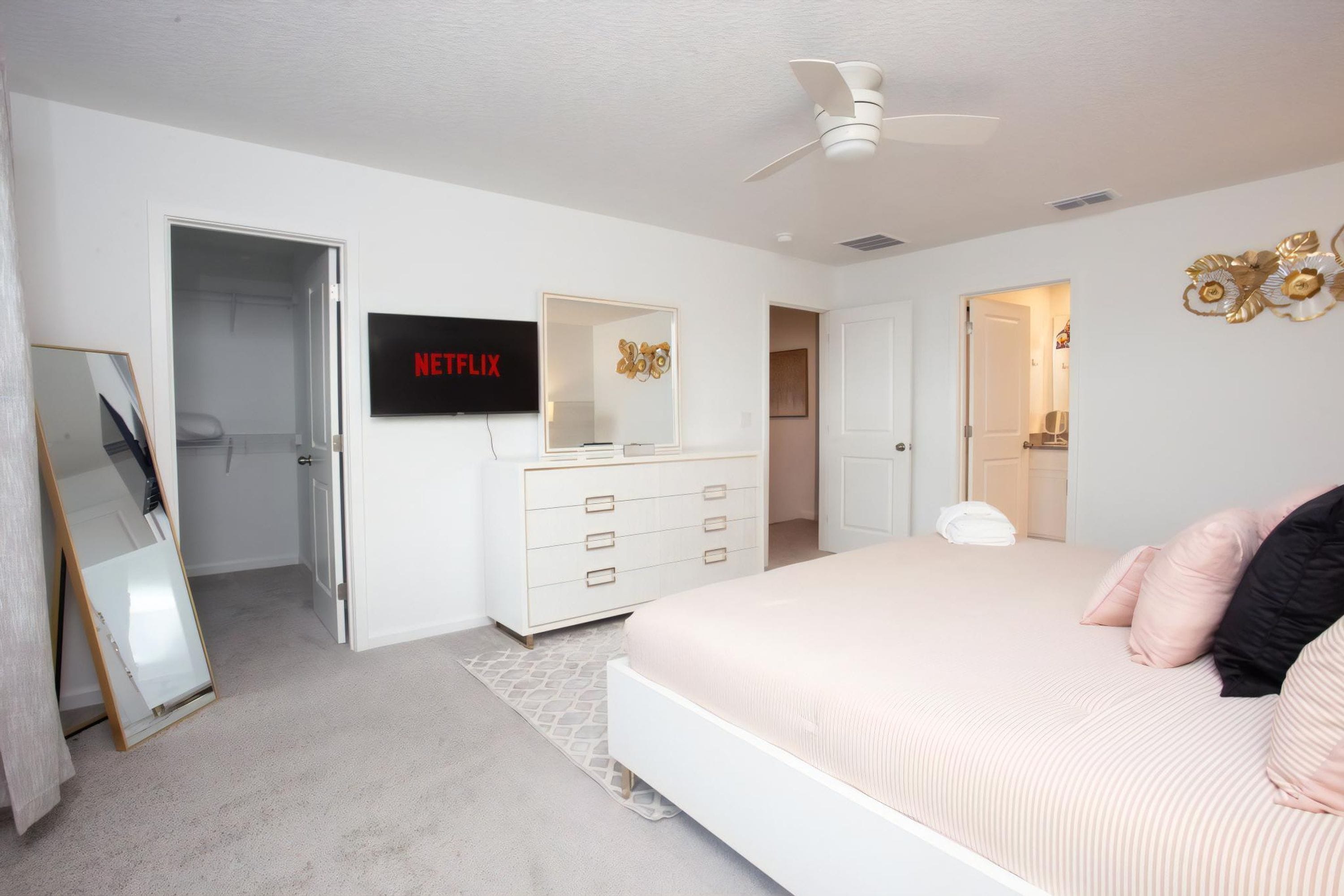 A bedroom with a bed, a dresser, a mirror, a ceiling fan, and a TV displaying Netflix.