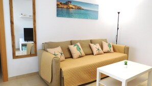 A living room with a beige sofa, a white coffee table, a painting of a coastal scene, and a floor lamp. - La Mar 2 in El Campello (El Campello)