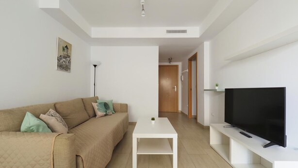 A modern living room with a beige sofa, a white coffee table, a flat-screen TV on a white stand, and a hallway leading to another room. - La Mar 2 in El Campello (El Campello)