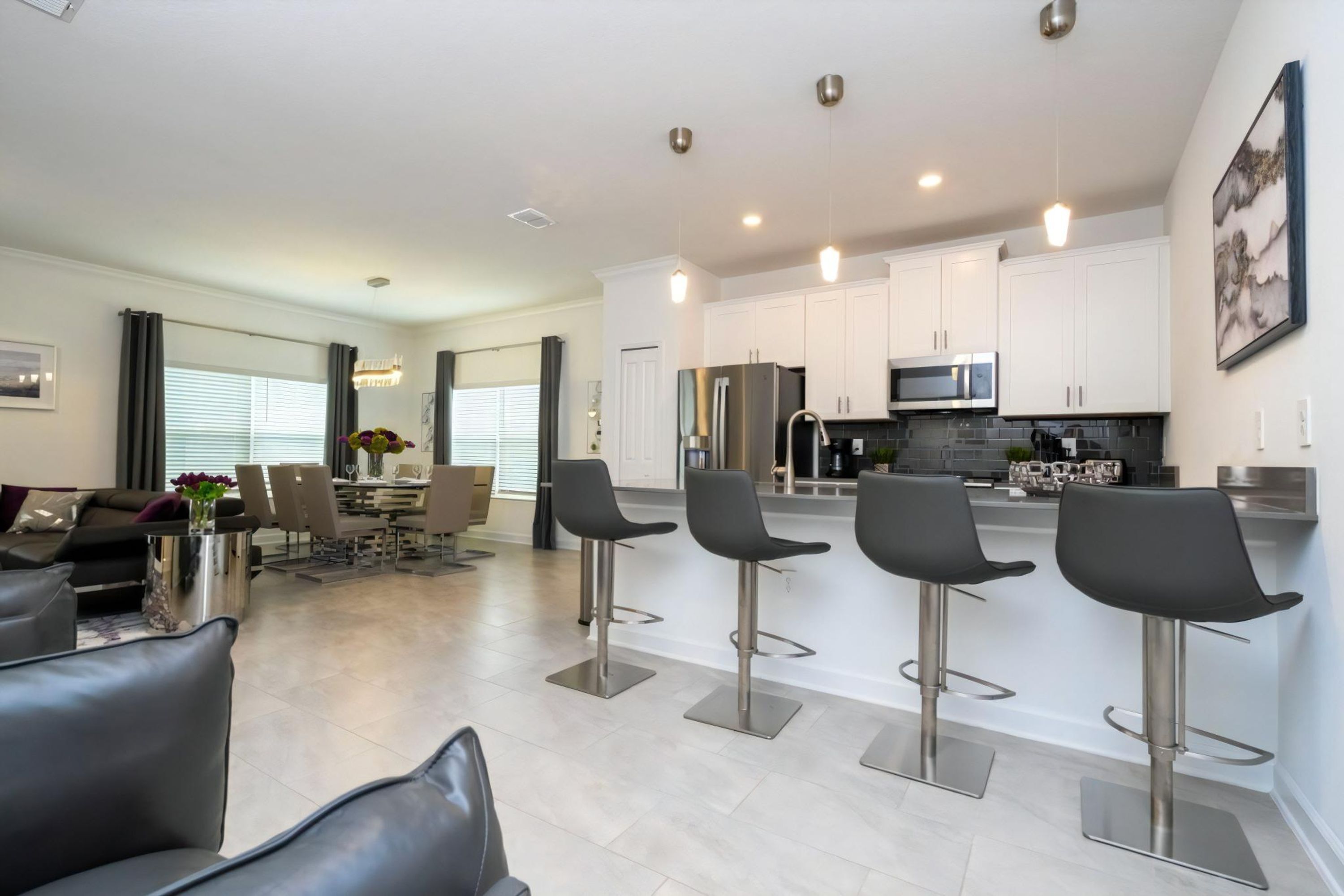 A modern kitchen with white cabinets, stainless steel appliances, and a bar area with black stools.