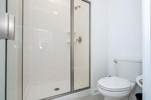 Ein Badezimmer mit einer Glaskabine zur Dusche, einer weißen Toilette und einem weißen Waschbecken.