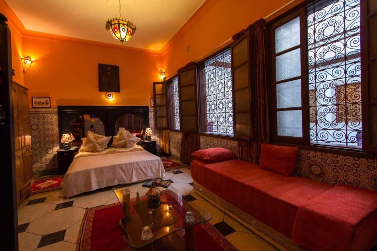 Una habitación con una cama, un sofá, una mesita de noche, una lámpara y un candelabro.