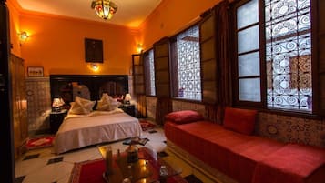 A room with a bed, a sofa, a nightstand, a lamp, and a chandelier.