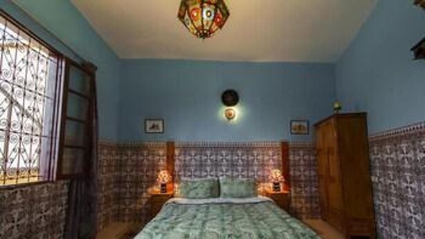 A bedroom with a bed, a window with bars, a wall clock, and a decorative ceiling light. - Riad Dar Ahl Tadla Fes (Fes)