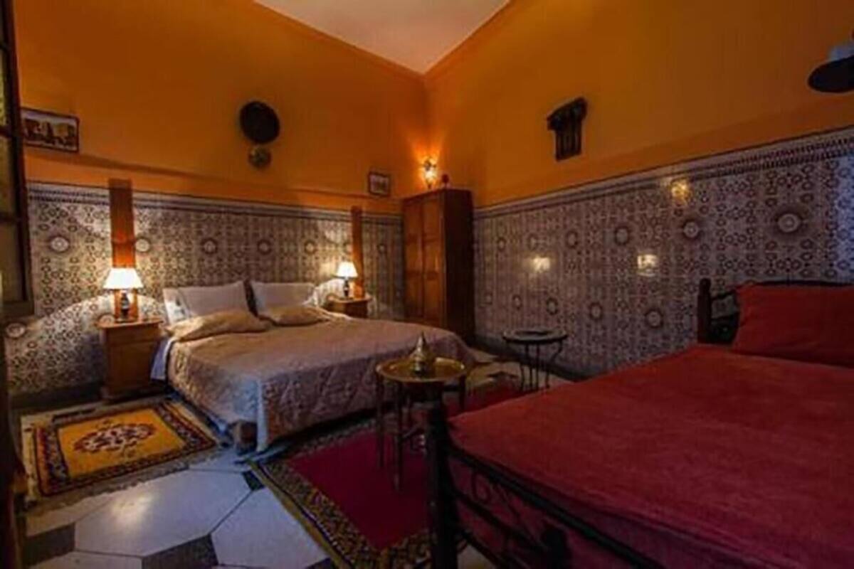 Habitación de hotel con dos camas, paredes con estampado y una mesita con lámpara.