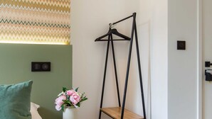 A bedroom with a bed, a bedside table with a vase of flowers, a wall-mounted light, and a black hanger stand. - Bright Studio - 2P - Beaugrenelle/eiffel Tower (Paris)