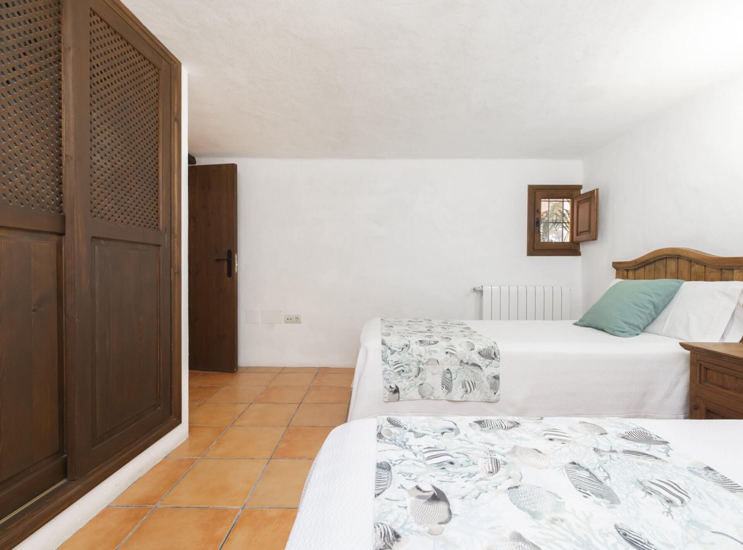 Un dormitorio con dos camas, un armario de madera, un radiador y un ventanal pequeño.