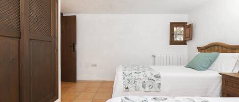 Un dormitorio con dos camas, un armario de madera, un radiador y un ventanal pequeño.