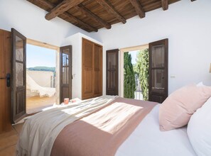 A bedroom with a large bed, wooden doors, and a view of the outdoors. - Villa Can Fumeral Modern and Seaview Salinas (Sant Antoni de Portmany)