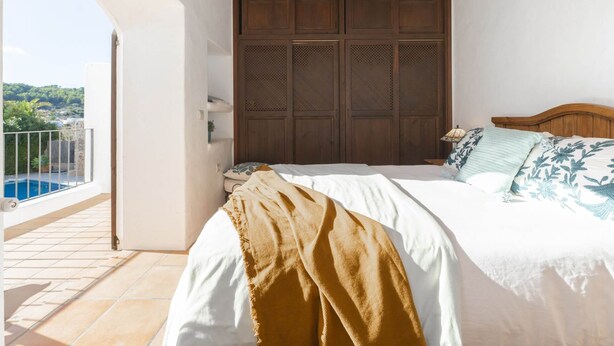A bedroom with a bed, wooden headboard, and a view of a pool. - Villa Can Fumeral Modern and Seaview Salinas (Sant Antoni de Portmany)