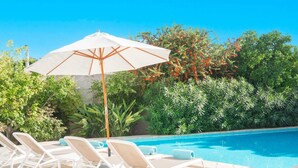 A pool area with lounge chairs and a white umbrella. - Villa Can Fumeral Modern and Seaview Salinas (Sant Antoni de Portmany)