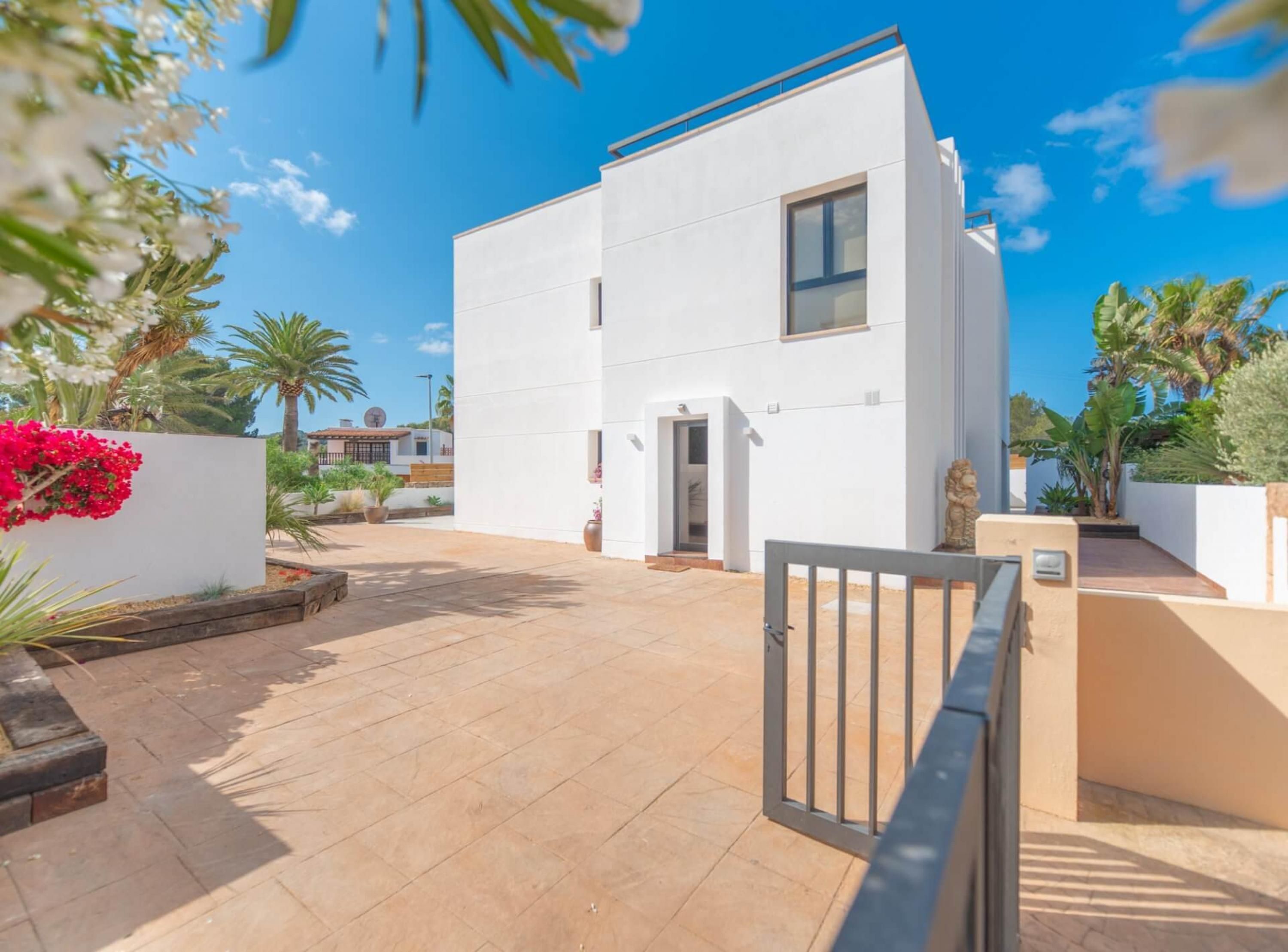 A modern two-story building with a flat roof, a small balcony, and a gated entrance.