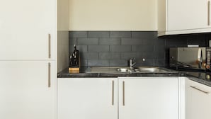 A modern kitchen with white cabinets, a black tiled backsplash, a stainless steel sink, and a microwave. - Cool Covent Garden 1BR - Netflix Nespresso (London)