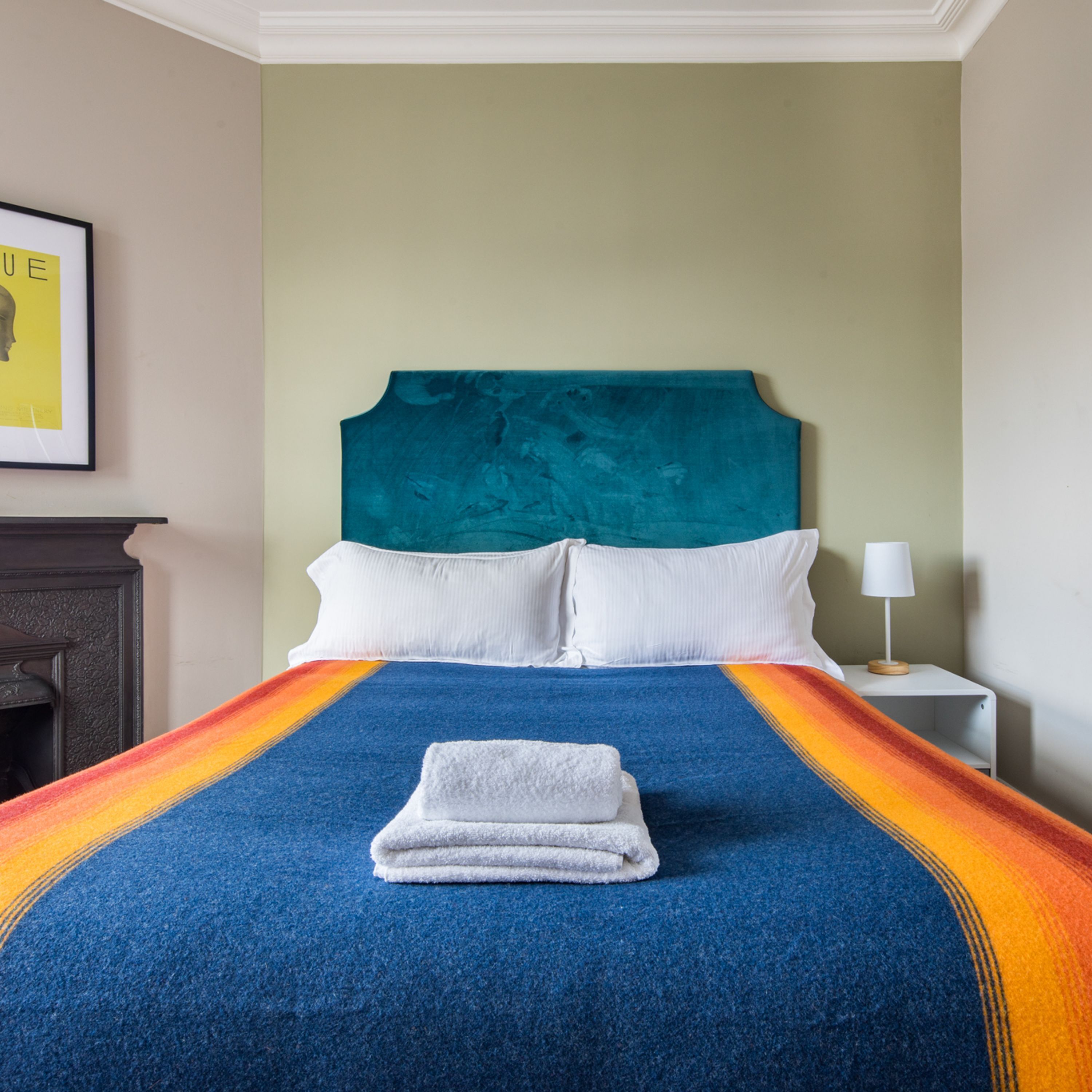 Een net opgemaakt bed met een blauw-oranje streepdeken en een gevouwen witte handdoek.