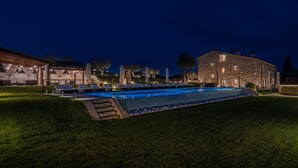 A swimming pool with lounge chairs and umbrellas, surrounded by well-maintained grass and stone buildings.