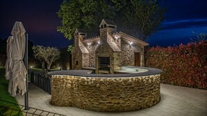 A stone building with a circular stone bench in front, surrounded by a fence and trees.