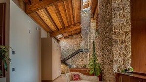 A cozy interior with a stone wall, wooden ceiling beams, a white sofa, and a staircase leading to an upper level.