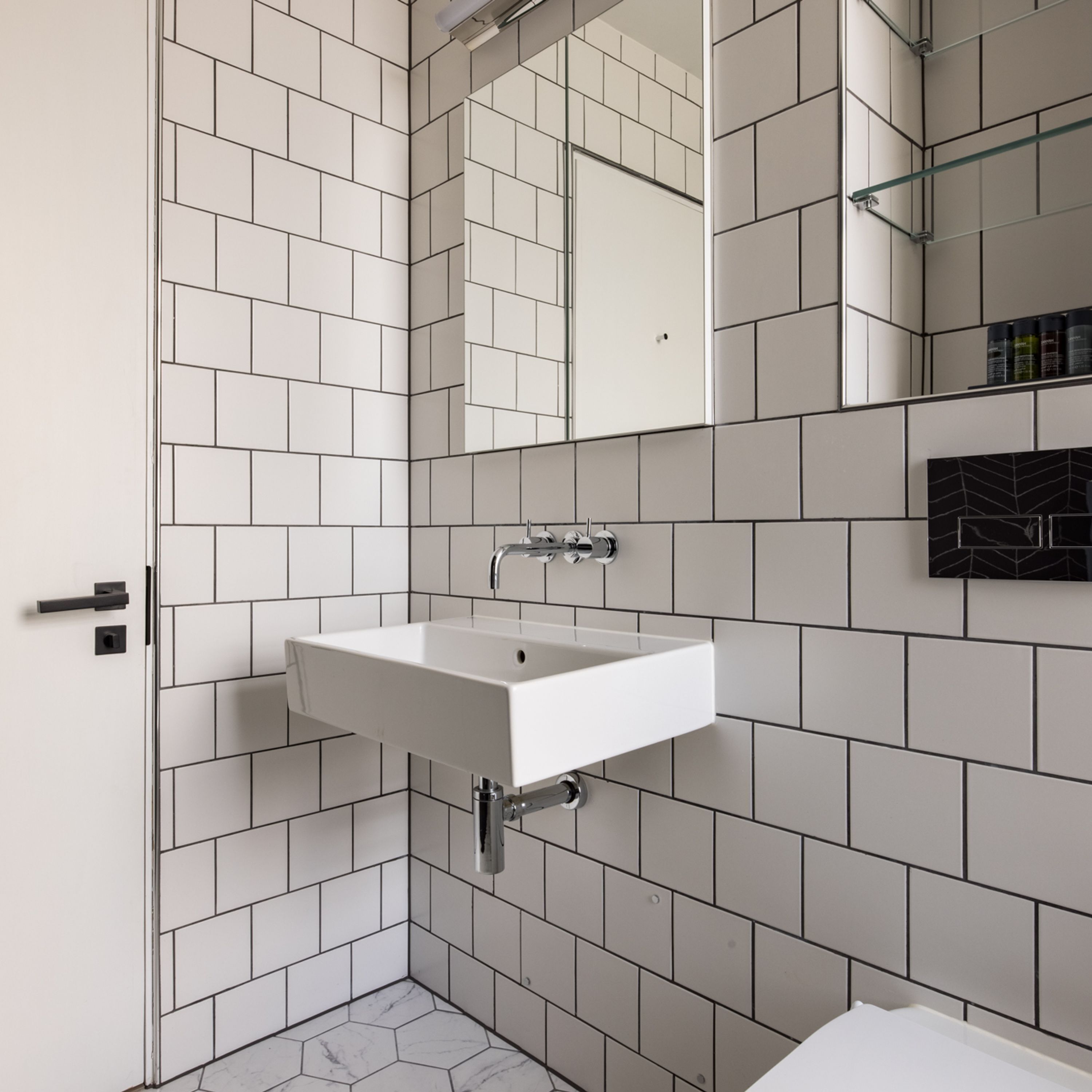 A bathroom with white tiled walls, a white sink, and a mirror above it.