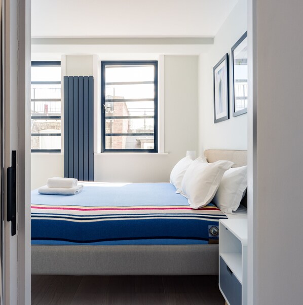 A modern hotel room with a bed, a window, a curtain, and a framed picture on the wall.