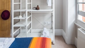 Une chambre avec une armoire blanche, une porte en bois, une fenêtre et un lit recouvert d’une couverture à rayures.
