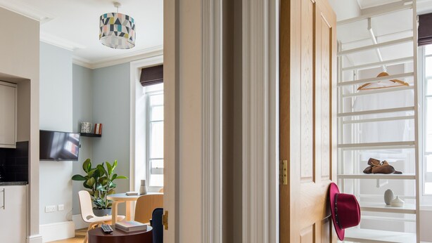 Un salon moderne avec un plancher en bois, un coin repas avec une table et des chaises, un téléviseur fixé au mur et un porte-chaussures contenant des chaussures et un chapeau.