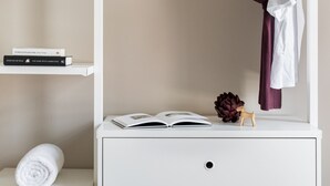 A neatly organized bedroom with a white dresser, a shelf with books, and a hanging clothes rack.