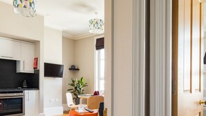 A modern kitchen with white cabinets, a black oven, and a dining area with a round orange table.
