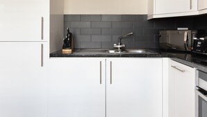 A modern kitchen with white cabinets, a black countertop, and a grey backsplash.