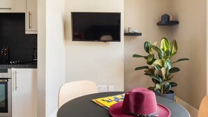 A modern kitchen with white cabinets, a black countertop, and a built-in oven. A round table with a black top and a pink hat on it is in the foreground.