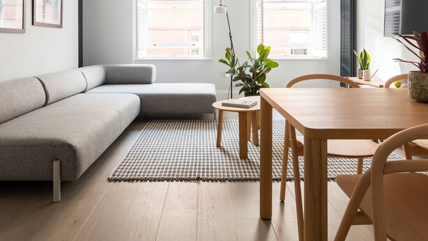 A modern living room with a sofa, a dining table, and a coffee table. There are two windows with blinds, a radiator, and a TV mounted on the wall. - Calm Leicester Sq 1BR - Netflix Nespresso (London)