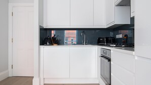 A modern kitchen with white cabinetry, a built-in oven, and a black coffee machine. - Calm Leicester Sq 1BR - Netflix Nespresso (London)