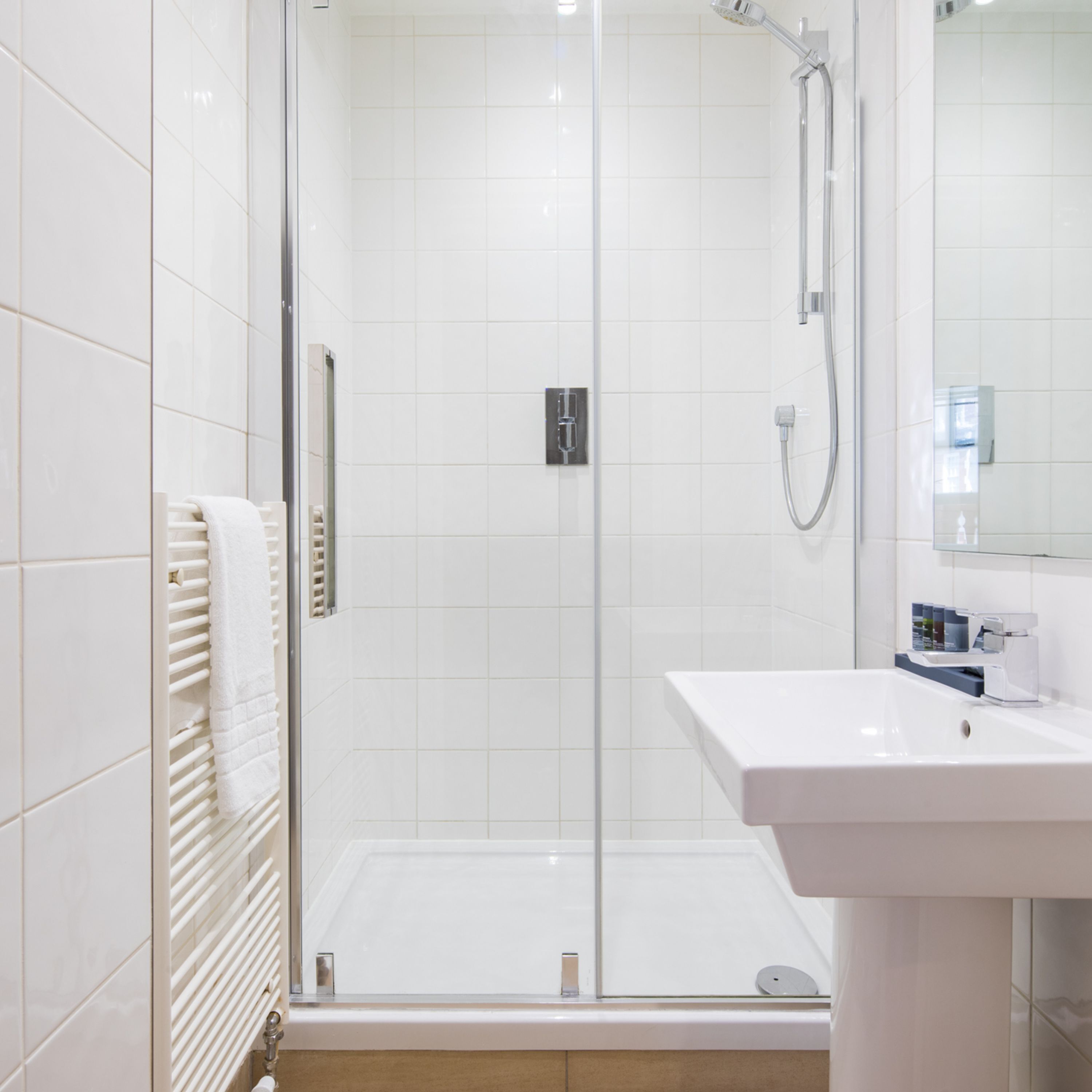 Ein modernes Badezimmer mit einer gläsernen Duschkabine, einem weißen Waschbecken und einem Handtuchhalter.