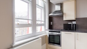 A modern kitchen with a built-in oven, microwave, and a window with curtains. - Funky Covent Garden Studio - Netflix Nespresso (London)