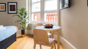 A hotel room with a bed, a dining table with chairs, a potted plant, and a television mounted on the wall. - Funky Covent Garden Studio - Netflix Nespresso (London)