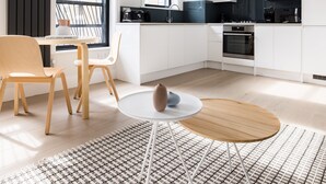 Een moderne keuken met witte kastjes, een zwart aanrecht en een ingebouwde oven. Er is een eethoek met een ronde tafel en twee stoelen.
