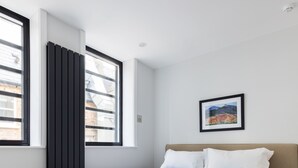Een hotelkamer met een bed, een raam, een radiator en een ingelijst kunstwerk aan de muur.