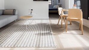 Een moderne woonkamer met een bank, een eettafel met stoelen, een aan de muur bevestigde televisie en een groot raam.