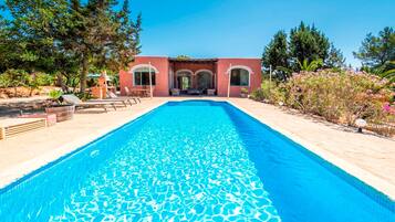 Una piscina con superficie d'acqua cristallina e blu, circondata da un giardino curato con diverse piante e alberi.