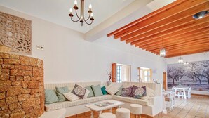 A spacious living area with a stone wall, a white sofa with cushions, a coffee table, and a wooden ceiling.