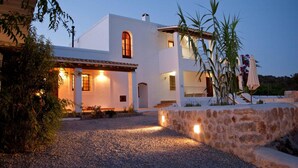 A two-story white building with a stone wall and gravel driveway.